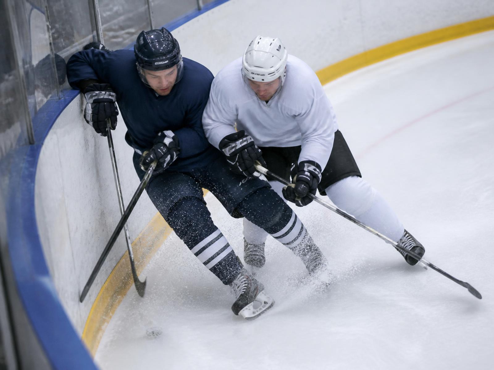 Two players battling for the puck along the boards in the defensive zone corner